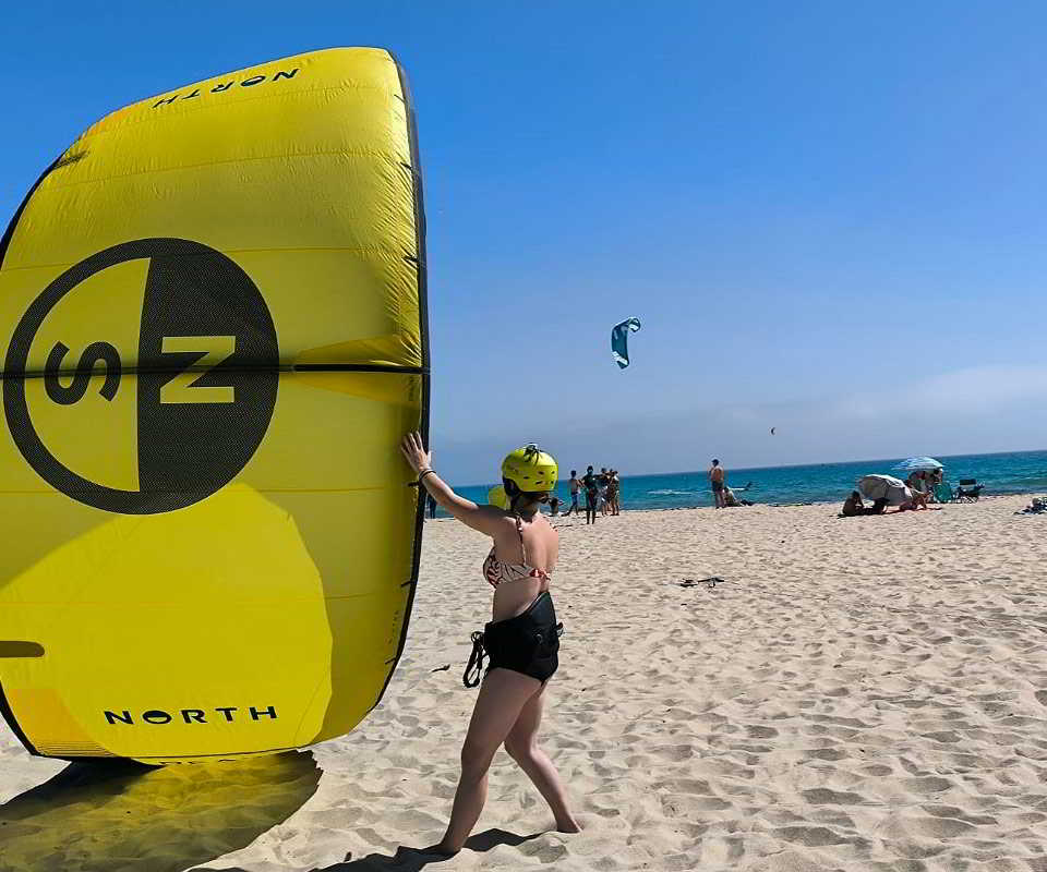Mujer con casco amarillo sosteniendo una cometa de kitesurf en la playa de Tarifa.