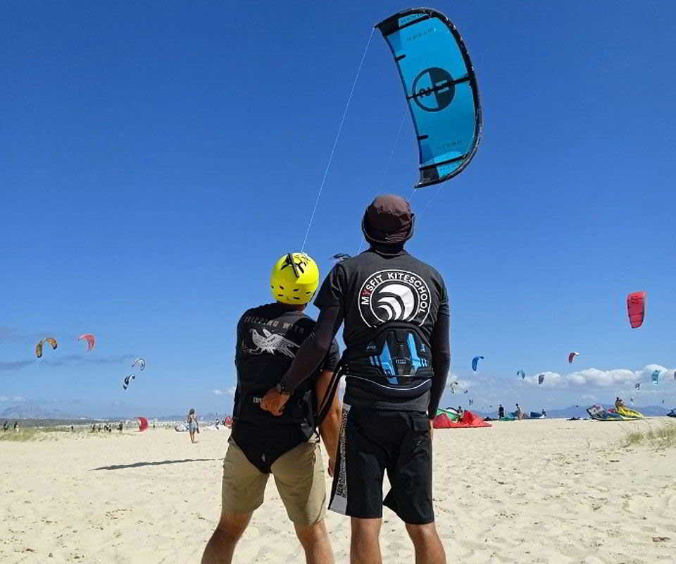Instructor enseñando a un alumno a manejar la cometa en la playa de Tarifa.