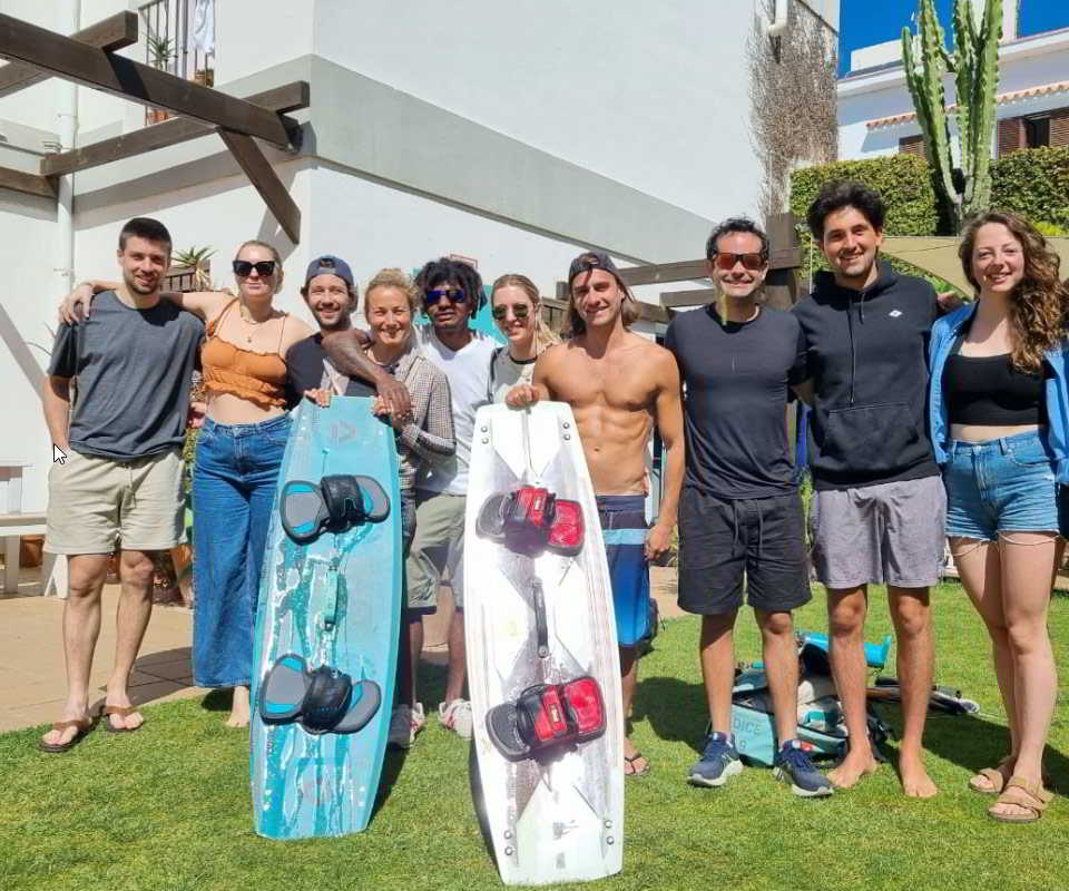 Grupo de alumnos y monitores de Mysfit Kite School posando con tablas de kitesurf en un jardín soleado.